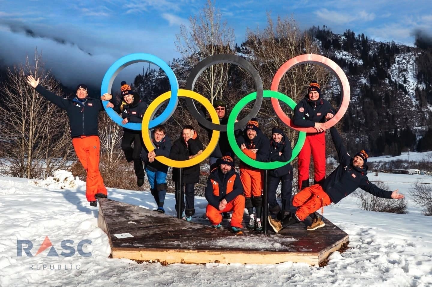 Kadra RASC Republic pozuje przy kołach olimpijskich na tle ośnieżonej doliny