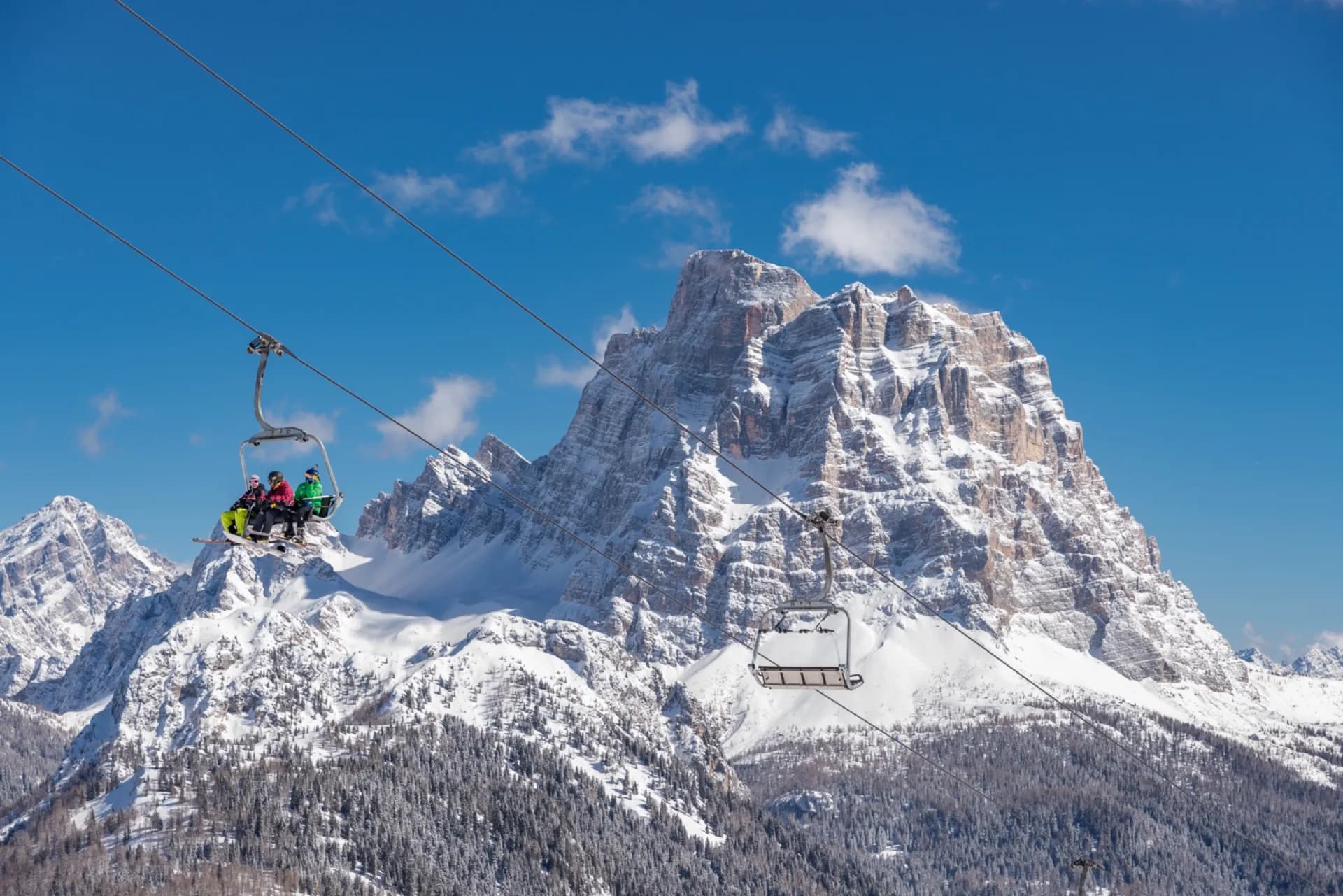 Narciarze na krzesełku wyciągu, w tle ośnieżony masyw Dolomitów