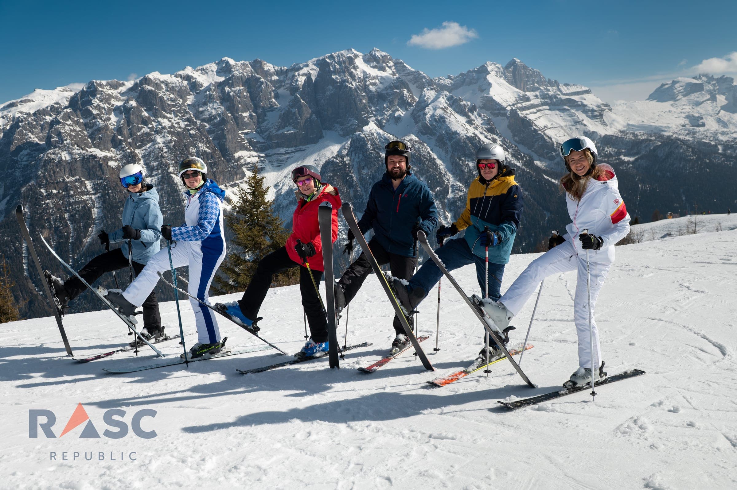 Sześcioro dorosłych narciarzy pozuje na stoku Val di Fiemme, w tle skalna panorama Dolomitów