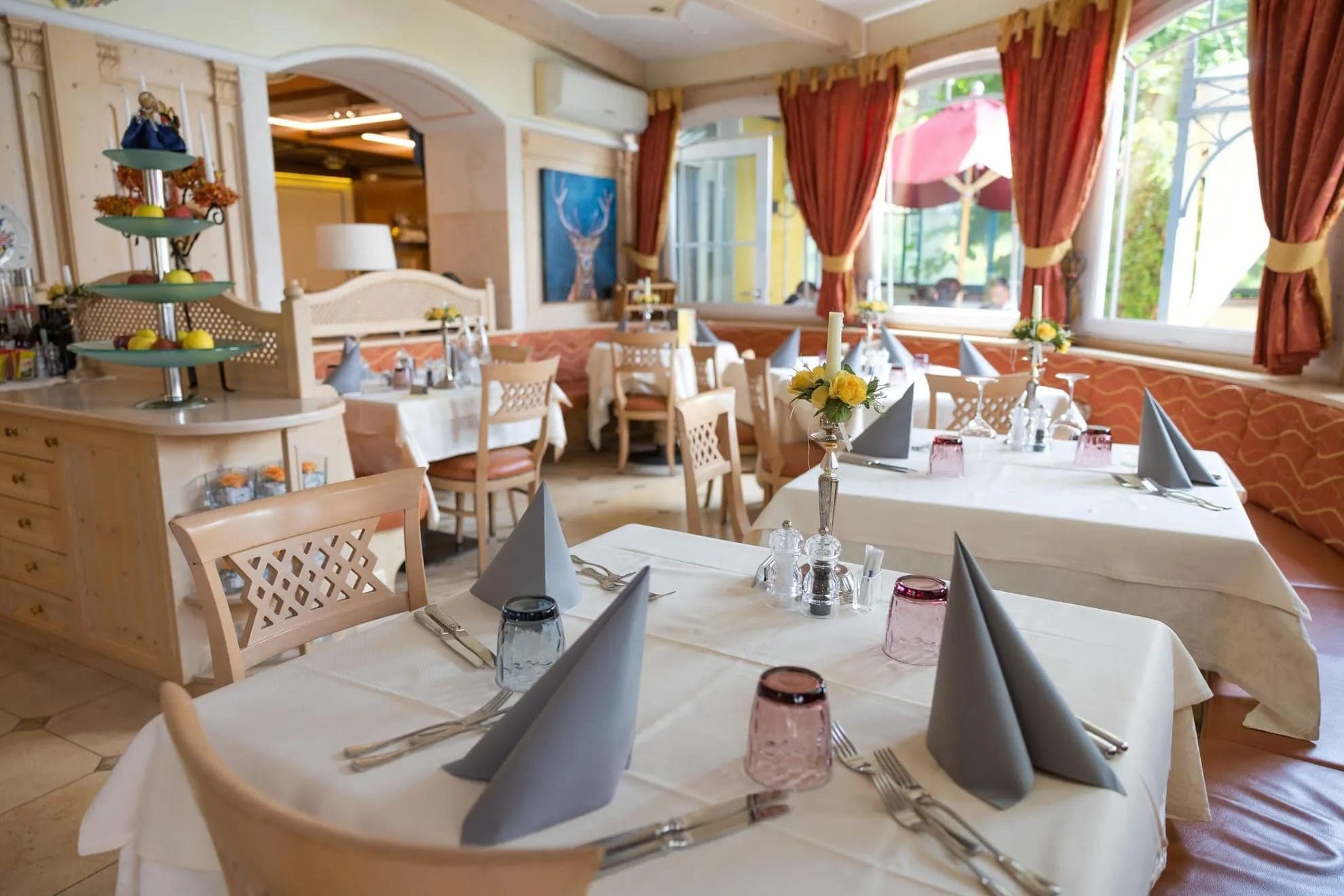 Hotelowa restauracja ze stołami nakrytymi białymi obrusami, jasne drewniane krzesła i okna na ogród