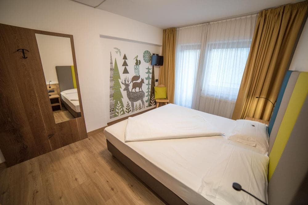 Pokój rodzinny w hotelu Olimpionico z leśną grafiką na ścianie i dużym łóżkiem