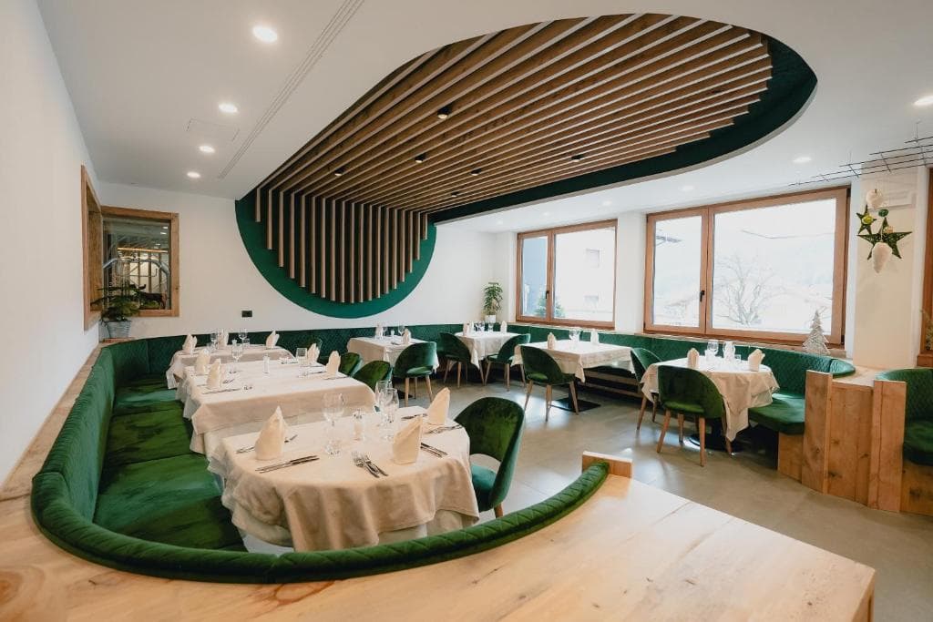 Restauracja hotelu Olimpionico z zielonymi kanapami, drewnianym podwieszanym sufitem i nakrytymi stołami