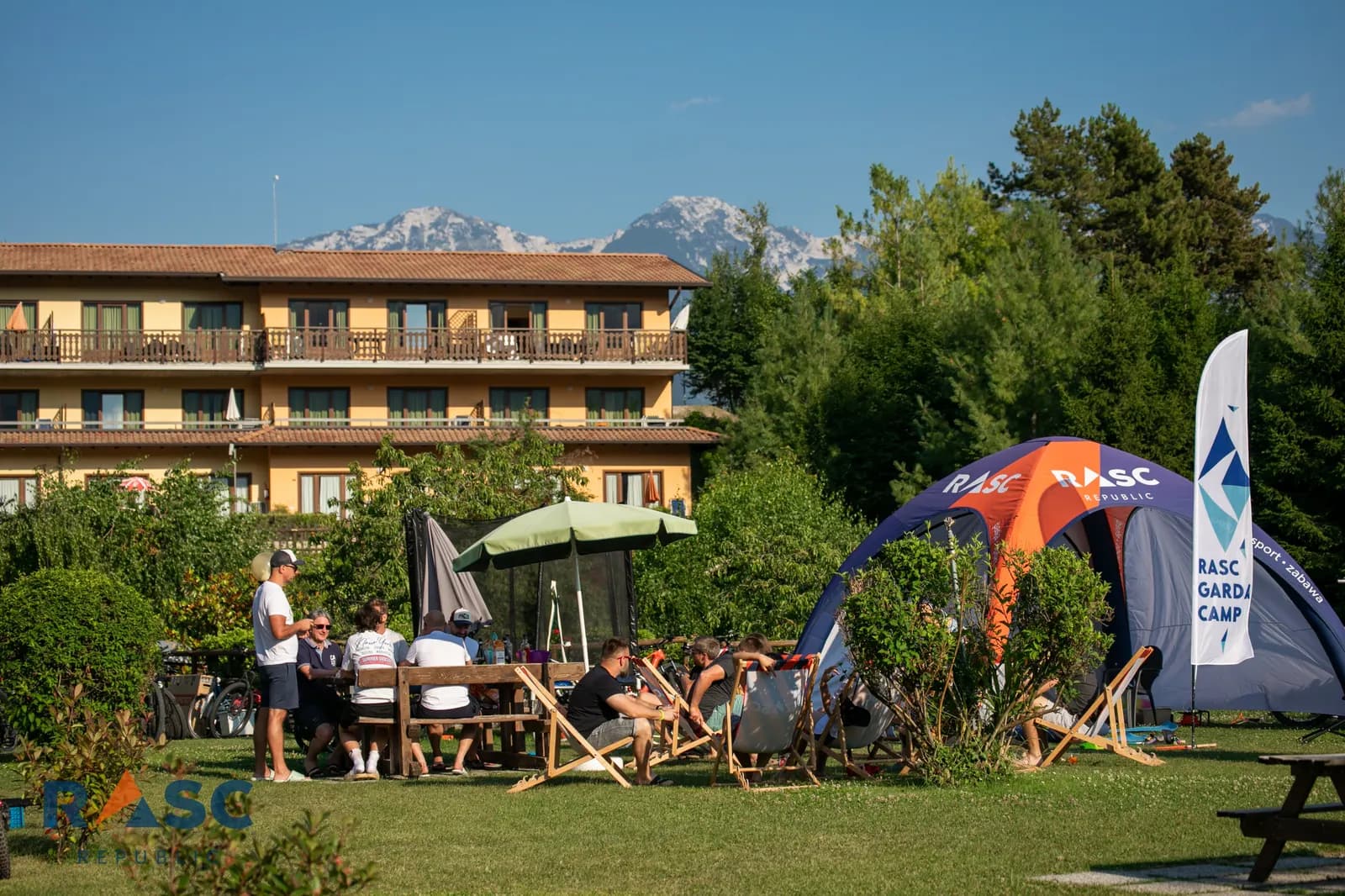 Uczestnicy RASC Garda Camp przy stołach i leżakach w hotelowym ogrodzie, obok namiot RASC, w tle budynek hotelu