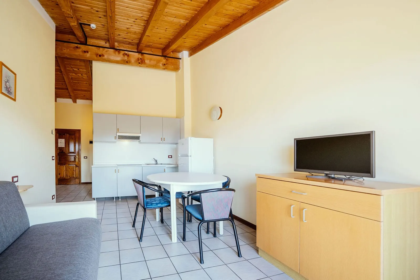 Salon apartamentu z aneksem kuchennym, stołem i telewizorem pod drewnianym stropem