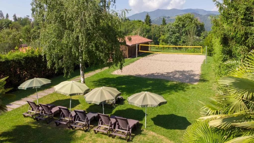 Leżaki pod parasolami na trawie, za nimi boisko do siatkówki plażowej