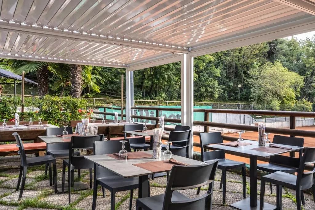 Stoliki na zadaszonym tarasie restauracji, za balustradą zieleń