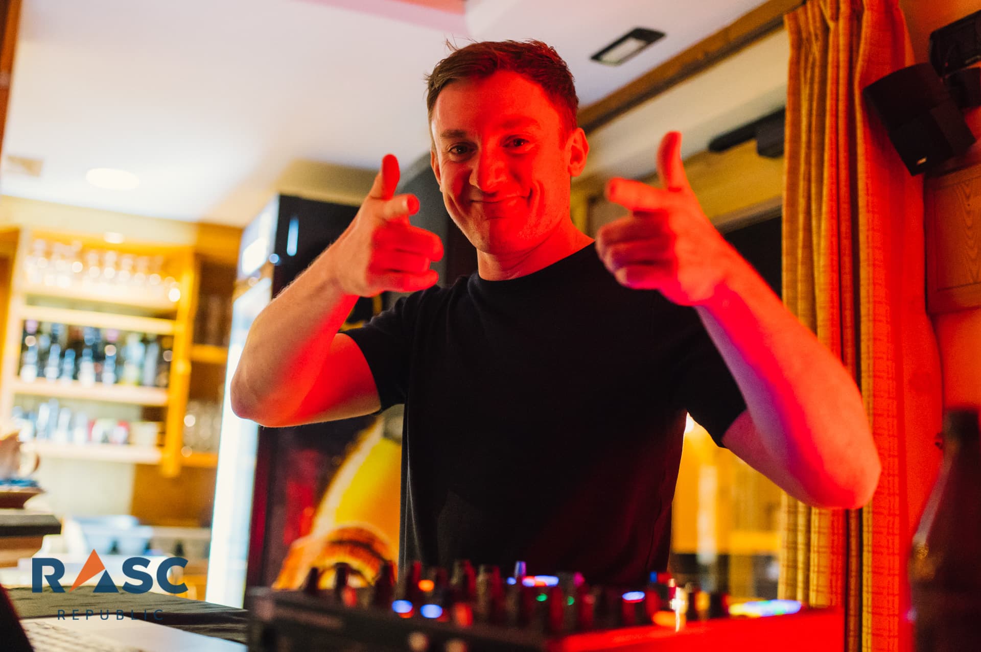 DJ za konsoletą w czerwonym świetle unosi oba kciuki w górę