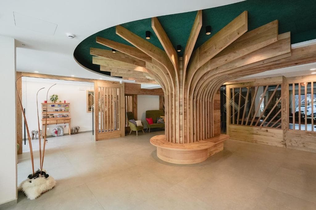 Lobby hotelu Olimpionico z rzeźbioną drewnianą kolumną w kształcie drzewa i nartami opartymi o ścianę