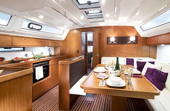 Wnętrze jachtu Bavaria Cruiser 46, mesa z drewnianym stołem nakrytym do posiłku, kanapą i kambuzem obok