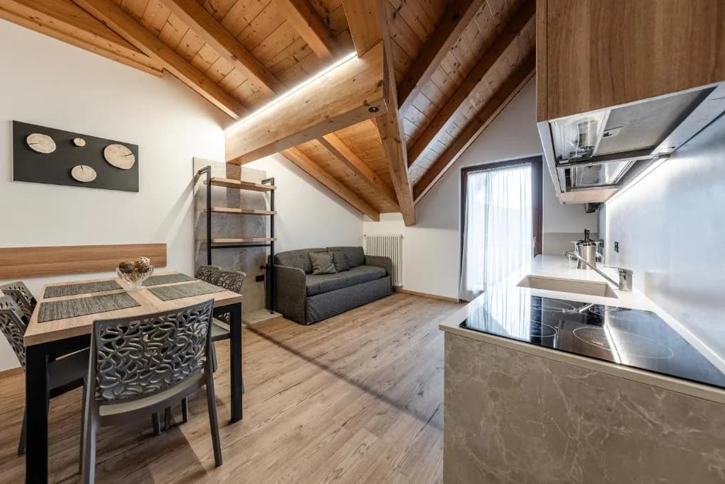 Salon apartamentu z aneksem kuchennym, stołem i sofą pod skosem drewnianego stropu