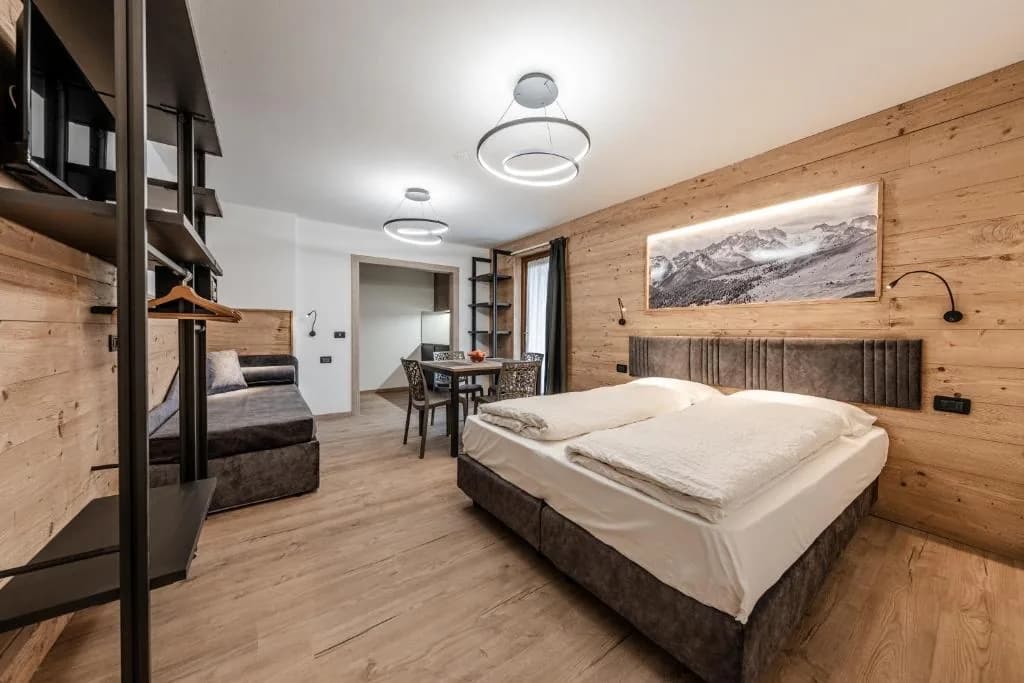 Sypialnia apartamentu z podwójnym łóżkiem i drewnianą zabudową, w tle salon