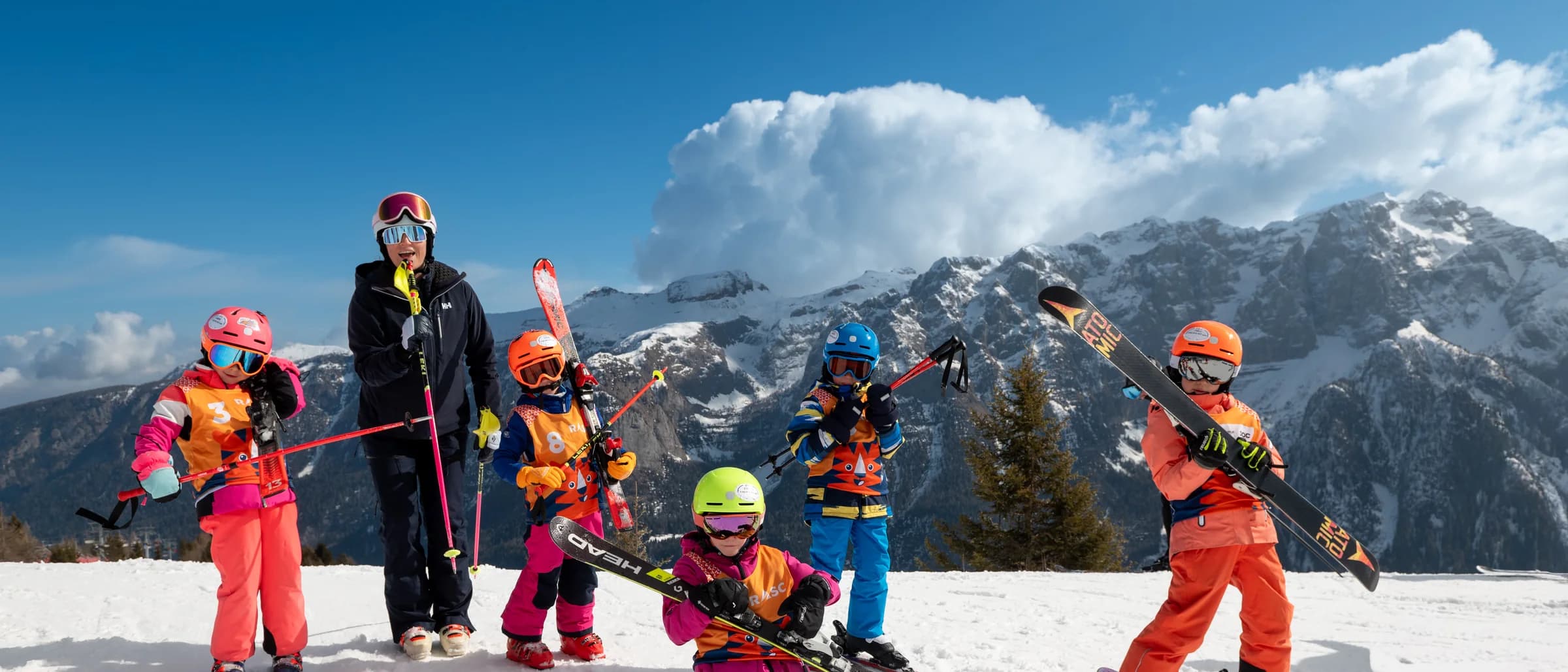 Sześcioro dzieci z nartami w rękach pozuje z instruktorką na stoku, w tle masyw Dolomitów Brenty