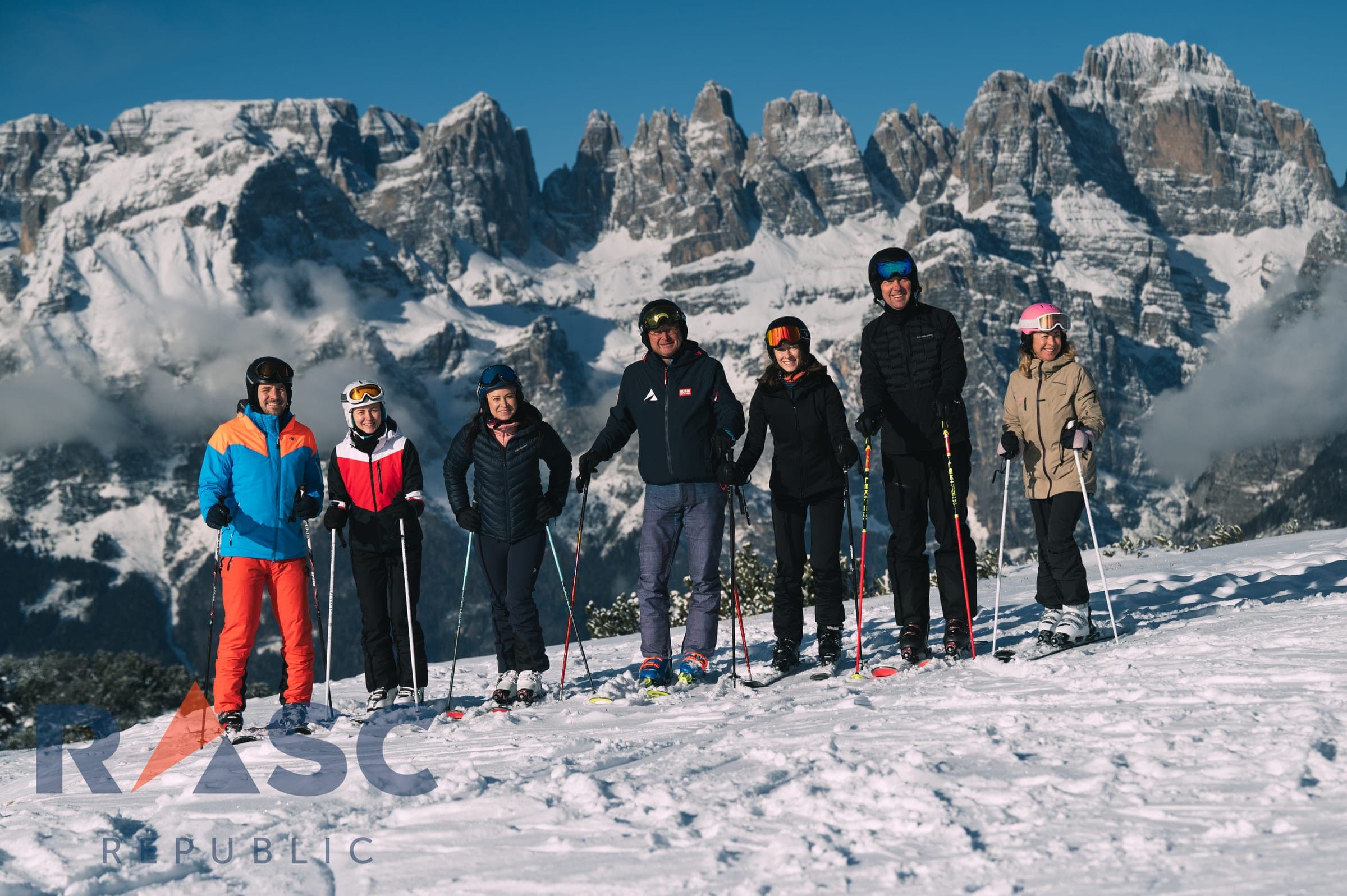 Grupa dorosłych uczestników szkolenia z nartami na stoku, w tle ośnieżona panorama Dolomitów Brenty