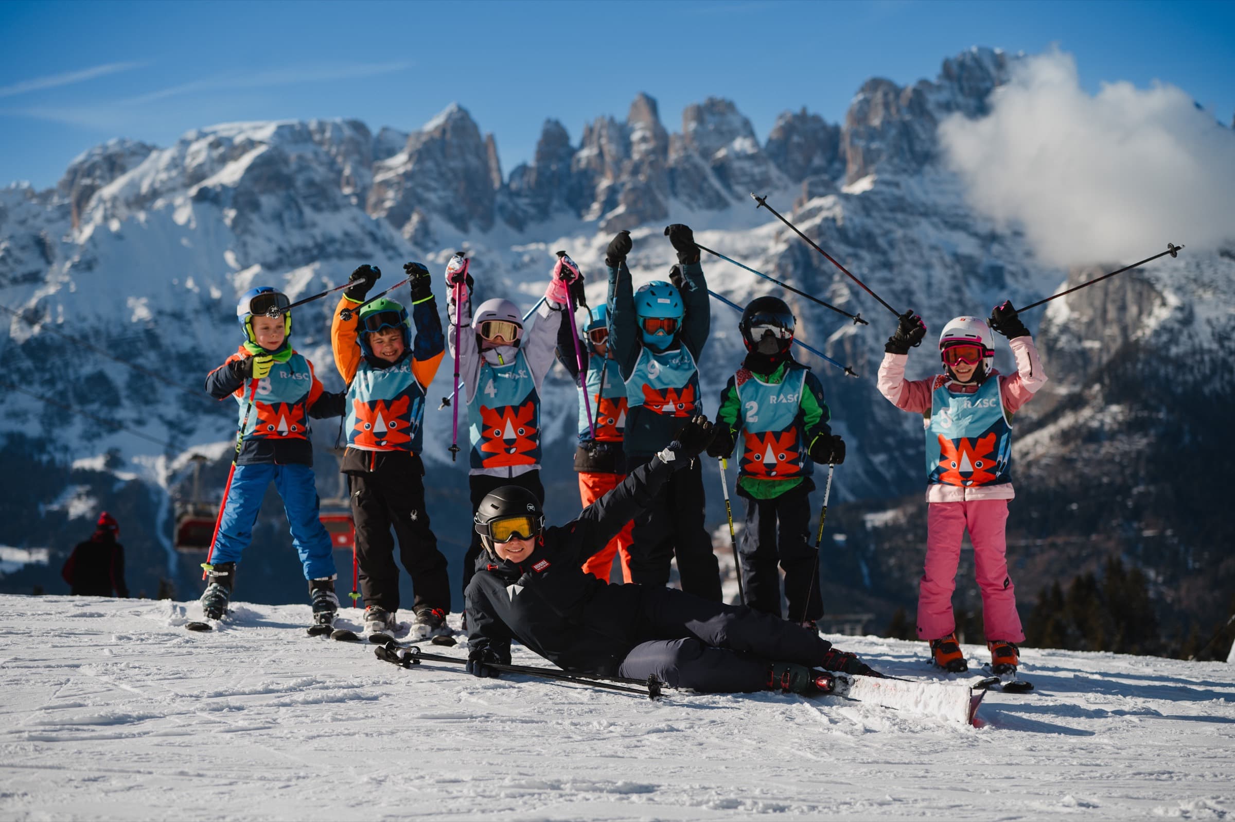 Grupa dzieci na nartach z instruktorem na stoku, w tle panorama Dolomitów